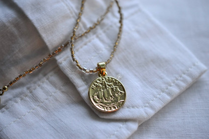 Lasihelmi kaulakoru kullatulla kolikko riipuksella.