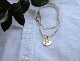 Lasihelmi kaulakoru kullatulla kolikko riipuksella.