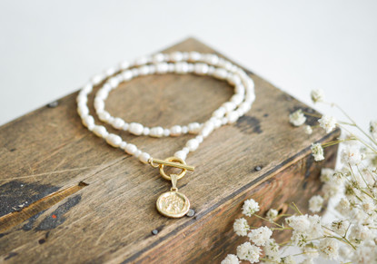 Helmikaulakoru kullatulla kolikko riipuksella.