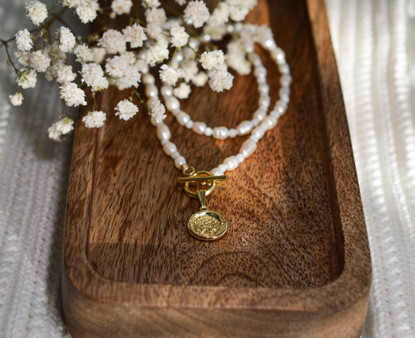 Helmikaulakoru kullatulla kolikko riipuksella.